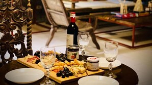 Une table à manger dressée avec une bouteille de vin, des verres et une variété de fromages et de fruits.