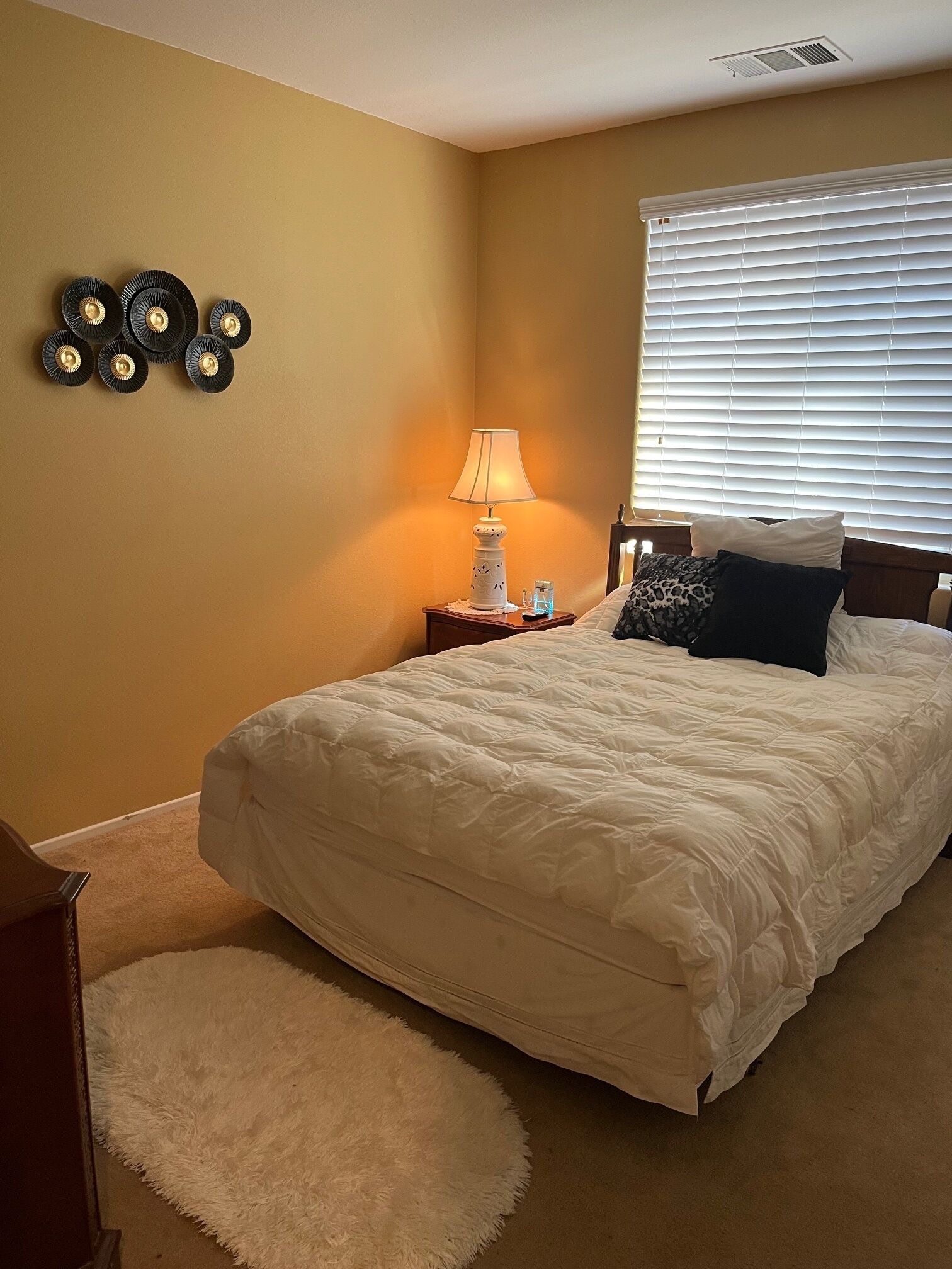 Een slaapkamer met een groot bed, een nachtkastje met een lamp en een decoratie aan de muur.