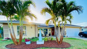 A residential house with a well-maintained lawn, palm trees, and a small decorative fountain. - Angie's Family-Favorite Lake Home: Heated Pool 3br/3ba (Port Richey)