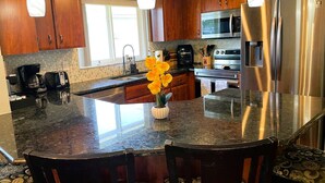 A kitchen with wooden cabinets, a granite countertop, stainless steel appliances, and a vase with flowers. - Angie's Family-Favorite Lake Home: Heated Pool 3br/3ba (Port Richey)