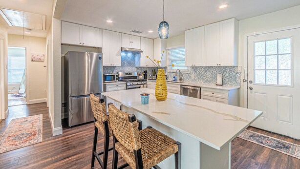 A modern kitchen with white cabinets, stainless steel appliances, and a central island with bar stools.