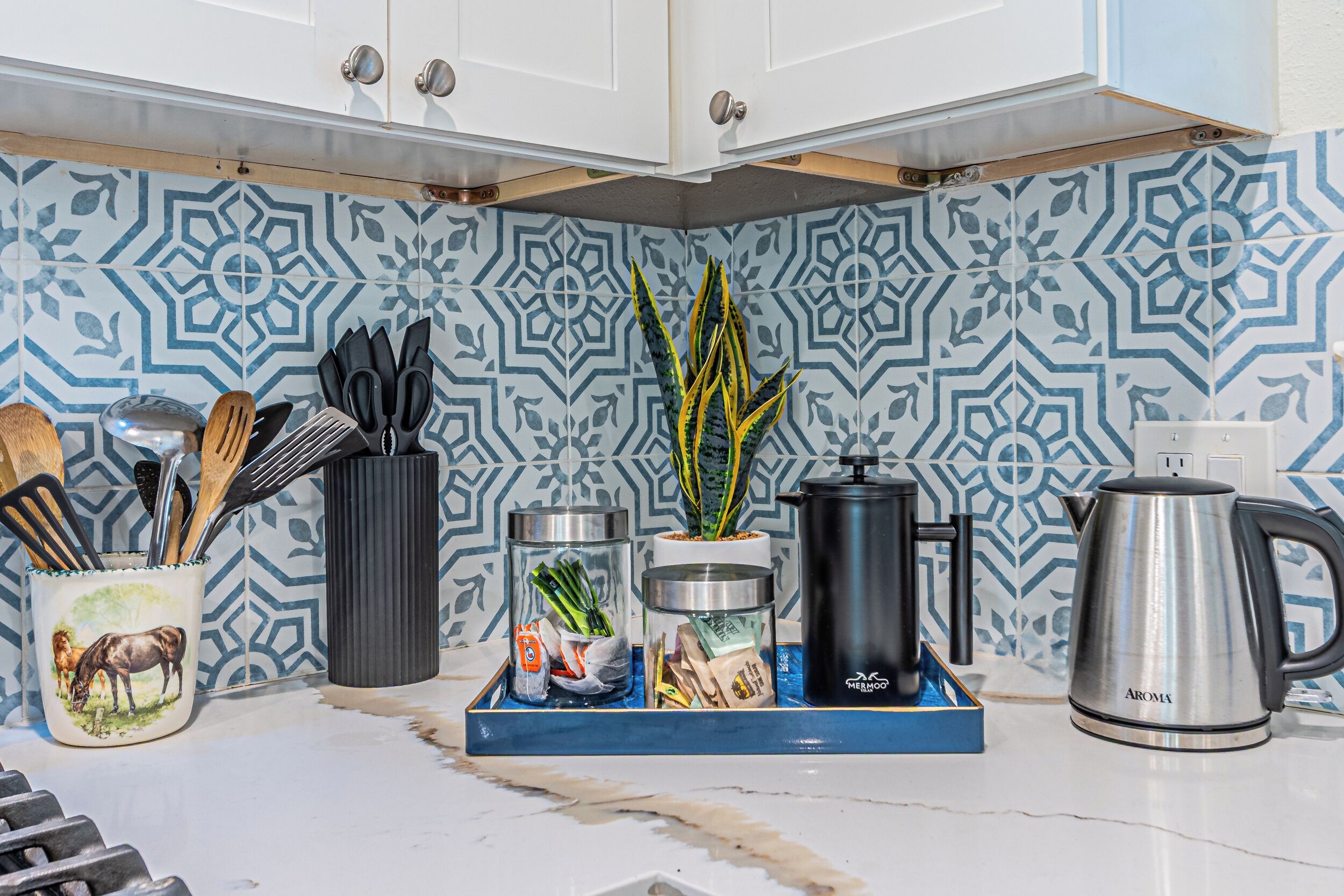 A kitchen with patterned tiles, a coffee maker, a kettle, and various kitchen utensils.