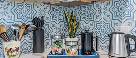 A kitchen with patterned tiles, a coffee maker, a kettle, and various kitchen utensils.