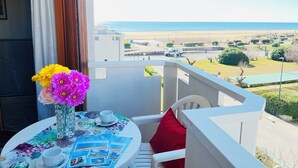 Een balkon met een tafel, bloemen en uitzicht op het strand.