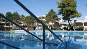 A clear swimming pool with a blue tiled floor, surrounded by trees and buildings in the background. - Flat with terrace overlooking the pool (Bibione)