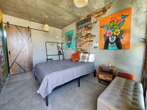 A bedroom with a bed, a small table, a bench, a wall-mounted air conditioner, and a painting. - 
“A Cabin Made for Escapes, Not Just Stays.” (Ejido El Porvenir (Guadalupe))