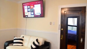 A living room with a black and white sofa, a flat-screen TV mounted on the wall, and a wooden door.