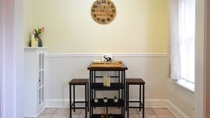 A room with a wooden clock on the wall, a white cabinet, and a small table with shelves.
