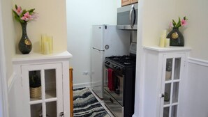 A narrow kitchen with white cabinetry, a stainless steel refrigerator, a stove, and a microwave. There are two vases with flowers on the countertops.