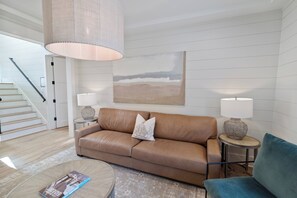 Ein modernes Wohnzimmer mit einem Ledersofa, zwei Beistelltischen mit Lampen, einem Couchtisch und einer Treppe.
