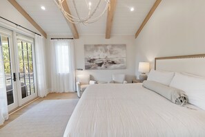 A bedroom with a large bed, a chandelier, a painting, and a view through the glass door.