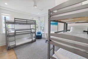 Ein Schlafraum mit Etagenbetten, Schreibtisch und Stuhl, großen Fenstern und einem Deckenventilator.