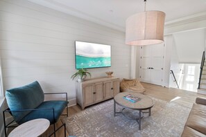 Ein modernes Wohnzimmer mit Flachbildfernseher, Sofa, Couchtisch und einer Pendelleuchte.