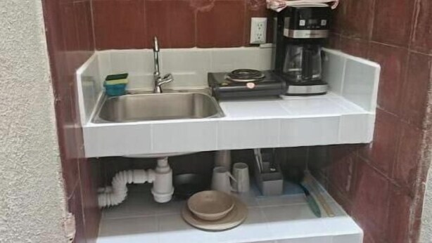 Een compacte keuken met een spoelbak, een koffiezetapparaat en een plank met servies.