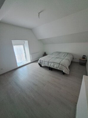 A spacious room with a large bed, a small bedside table, a nightstand, and a window with a view.