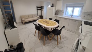 A modern kitchen with white cabinets, a dining table with chairs, a sofa, and a built-in washing machine. - Gite des moissons 41 near Chambord castle  (La Chapelle-Saint-Martin-en-Plaine)