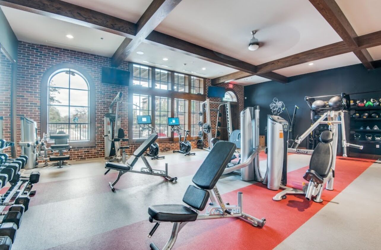A gym with various exercise equipment, large windows, and a brick wall.