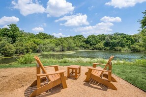 Vista di un fiume con una spiaggia sabbiosa in primo piano, con poltrone in legno di stile Adirondack e un tavolino.