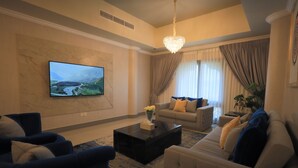 A modern living room with a flat-screen TV, a black coffee table, a beige sofa, and a blue armchair.