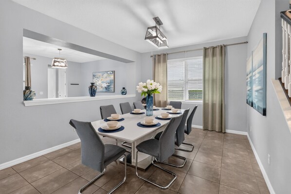 A dining room with a rectangular table set for six, surrounded by grey chairs.