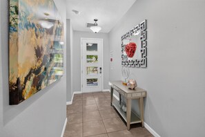 A hallway with a door, a console table with a geometric mirror, and a large abstract painting.