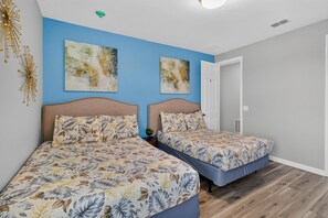 A bedroom with two beds, a blue accent wall, and two abstract paintings.