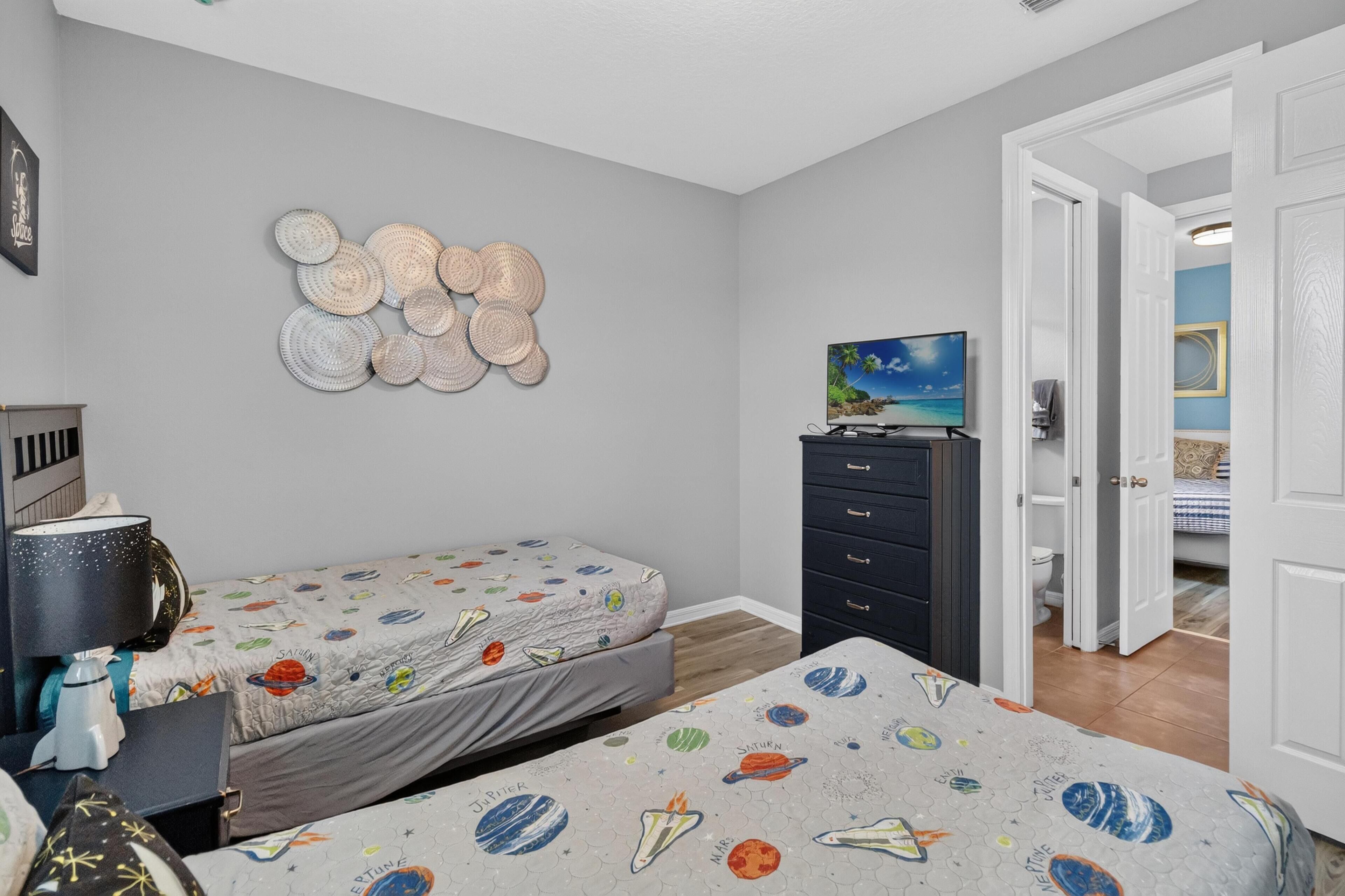 A bedroom with two beds, a dresser, a television, and a wall decoration.