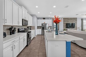 A modern kitchen with white cabinetry, a central island, and a dining area with a sofa.