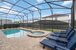 A pool area with a hot tub, lounge chairs, and a covered patio.