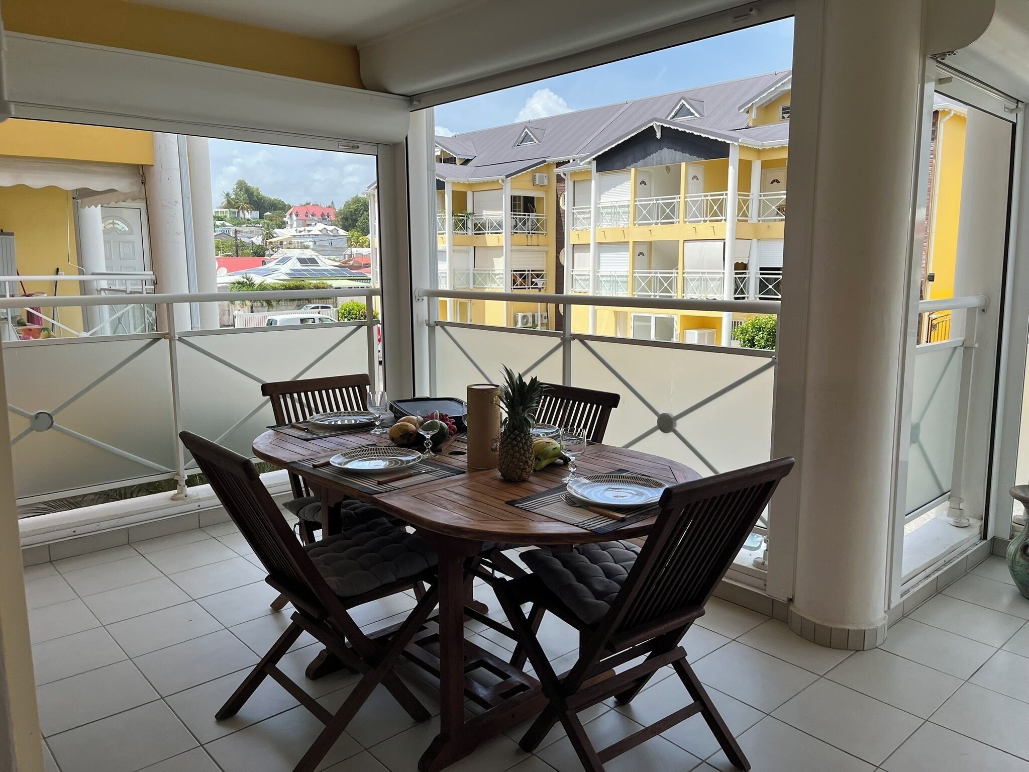 A dining area with a table set for four, chairs, and a view of a yellow building with balconies.
