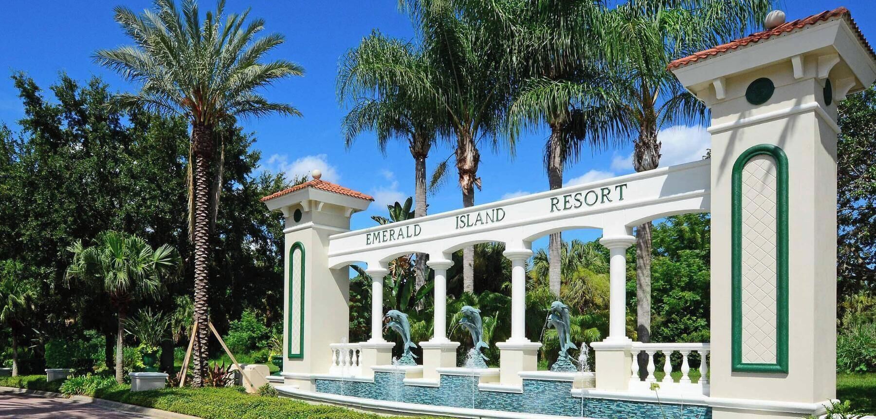 Ein weißer Eingangsbogen mit der Aufschrift 'Emerald Island Resort' und Delfinstatuen.
