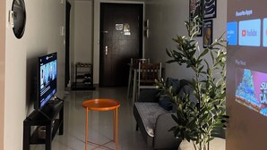A modern living room with a flat-screen TV, a small orange table, a sofa, and a potted plant.