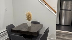 A modern kitchen with a stainless steel refrigerator, a dark wooden dining table with four chairs, and a staircase with a wooden handrail.