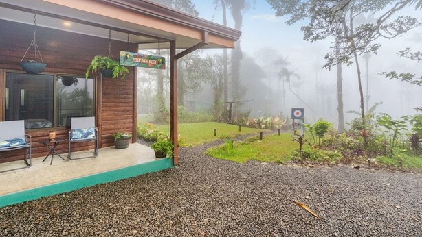 Un bâtiment moderne doté d’un espace extérieur couvert avec des sièges, d’une cible et d’un chemin qui traverse un jardin.