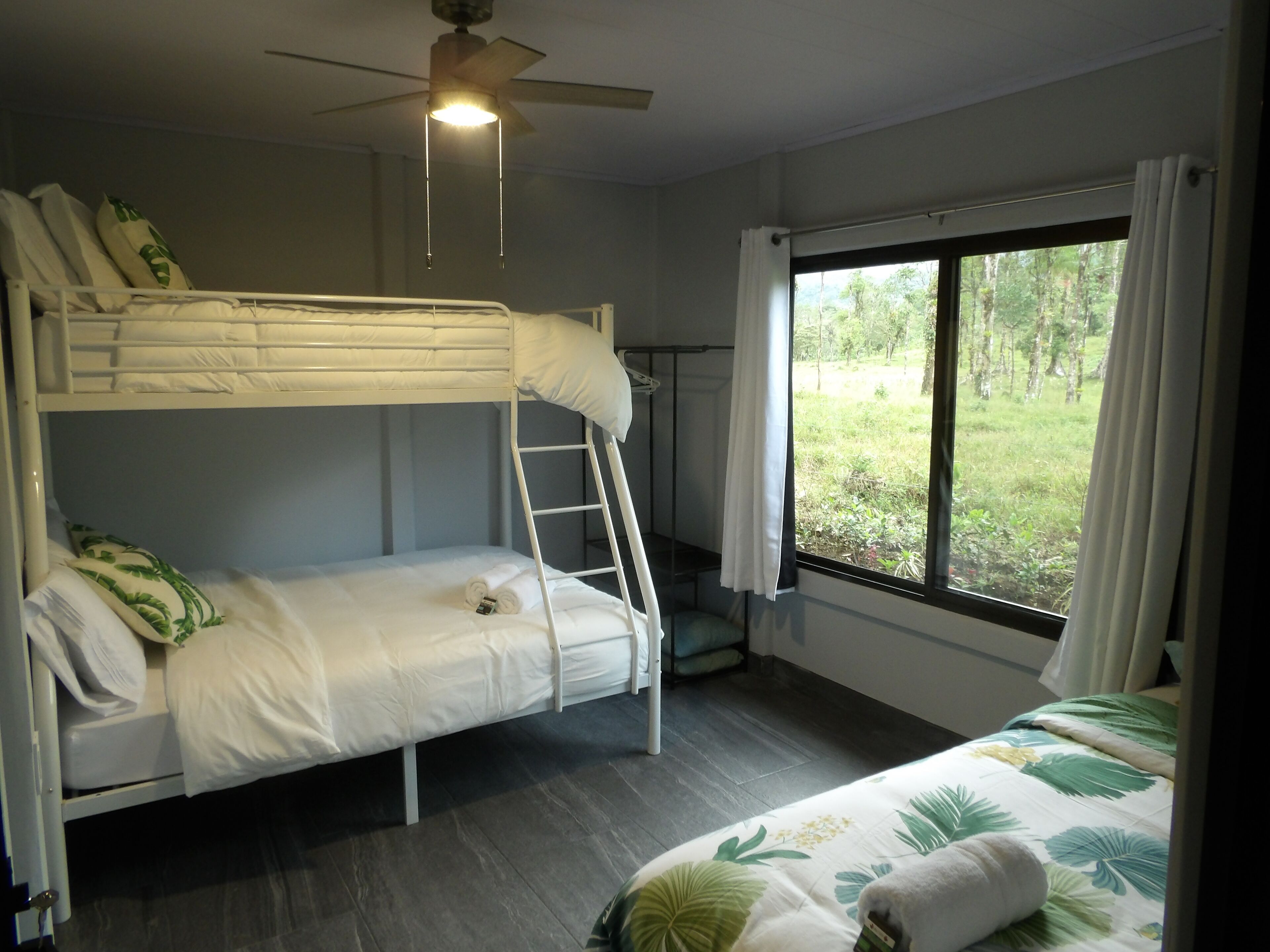 Habitación con literas, una escalera, ventilador de techo y ventana con cortinas.