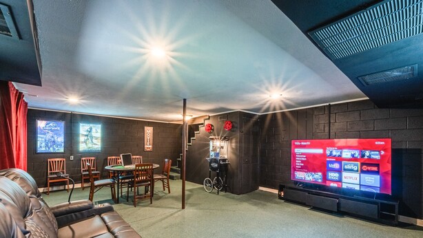 Ein modernes Wohnzimmer mit einer Ledersofa, einem Essbereich mit Holzsesseln, einem Fernseher, der verschiedene Sender zeigt, und einer Treppe, die zu einer oberen Ebene führt.