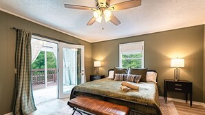 Ein Schlafzimmer mit einem Bett, einer Bank, zwei Nachttischen, einem Deckenventilator und Blick durch eine Schiebetür.