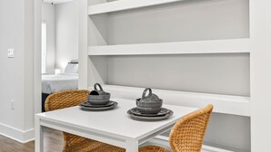 A modern, minimalist room with white walls, a white table, and wicker chairs. There are two dark ceramic teapots on the table. - Stylish 1BR in Heart of Midtown Tampa (Tampa)