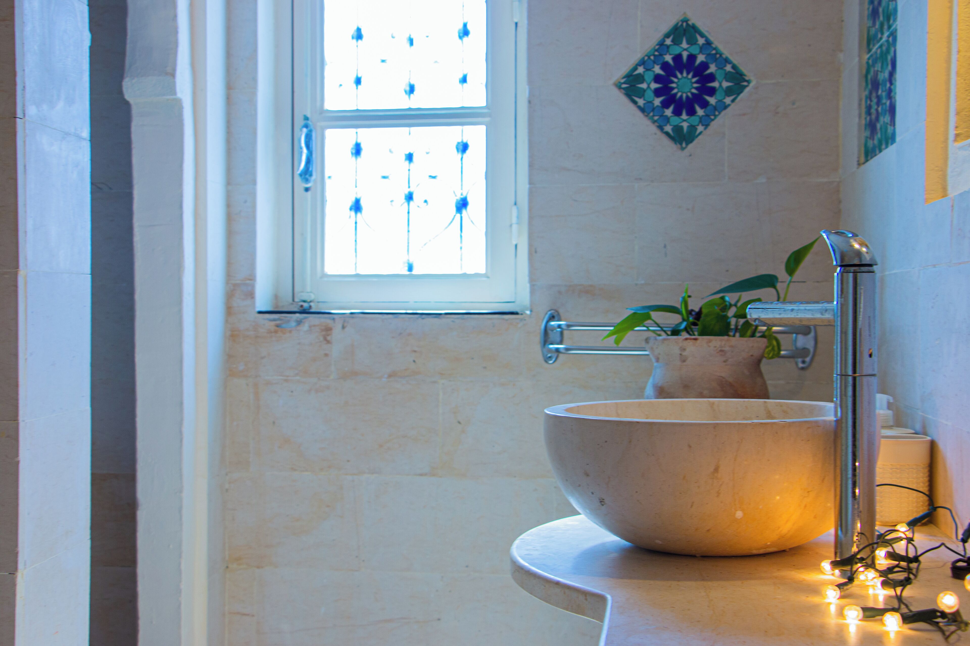 A bathroom with a large bowl sink, a window with decorative glass, and a potted plant.