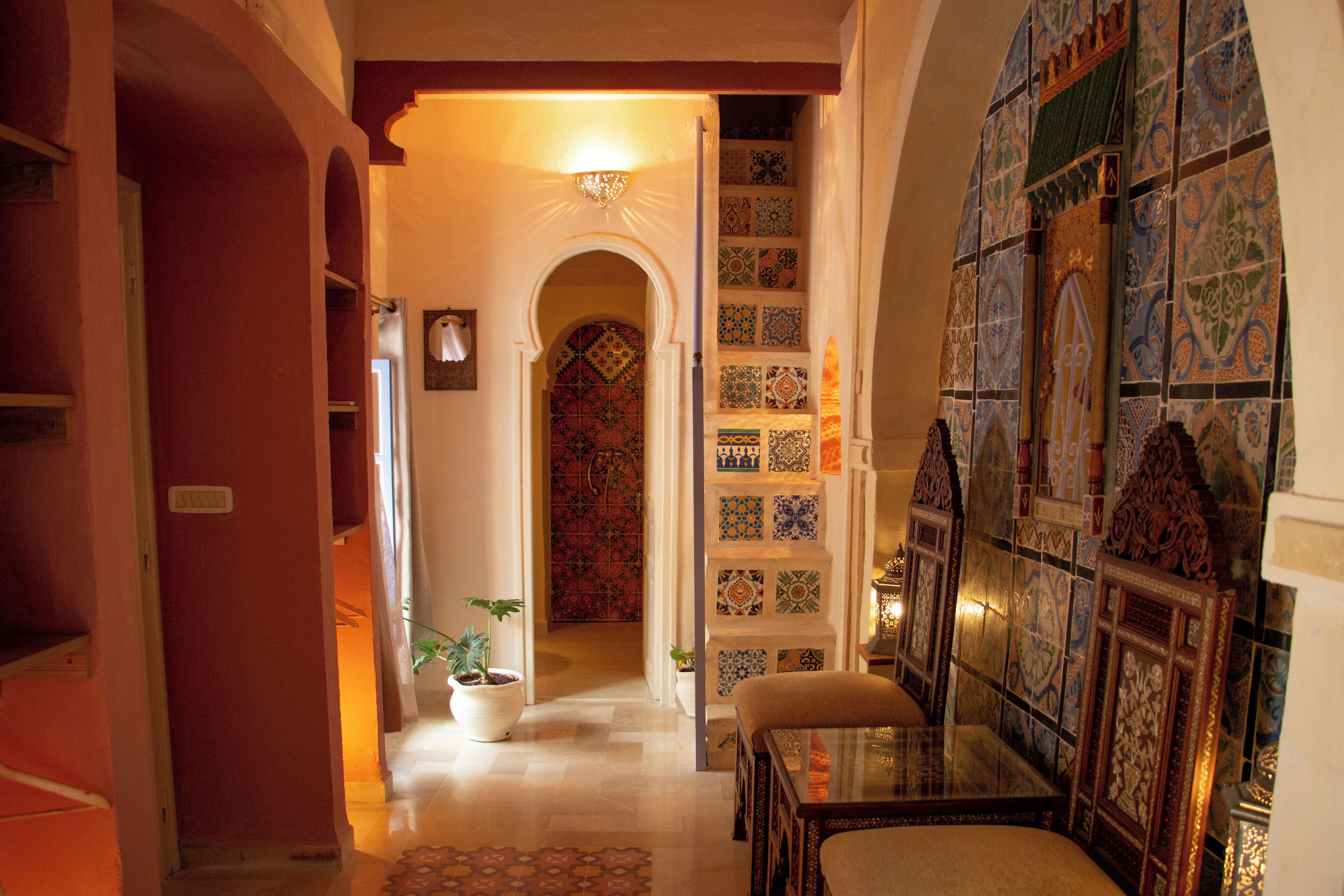 A hallway with a tiled wall, a door with a patterned door, and a small table with a chair.