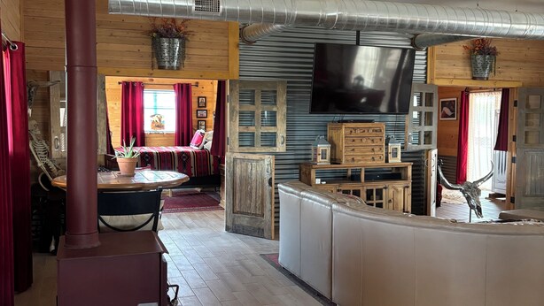 Un salon chaleureux avec un poêle à bois, une grande télévision et un ventilateur de plafond.