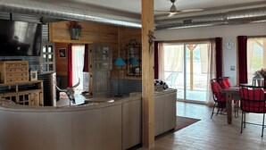 Un vaste espace de vie comprenant une grande table à manger en bois, un canapé et un coin cuisine équipé d’un téléviseur et de placards.