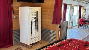 Une pièce avec un plafond en bois, un téléviseur à écran plat fixé au-dessus d’un réfrigérateur blanc, des rideaux rouges et un tapis à motifs.