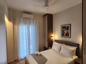 A hotel room with a bed, a nightstand, a wall-mounted air conditioner, a painting, and a window with curtains. - Smile in the the Center of Athens &Breakfast optional (Athina)