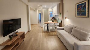 Uma sala de estar moderna com televisão de tela plana, piso de madeira, sofá e área de jantar com mesa e cadeiras.