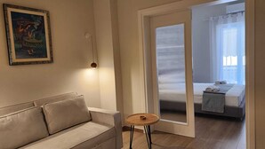 Uma sala de estar moderna com um sofá bege, uma mesinha redonda e uma obra de arte emoldurada na parede.