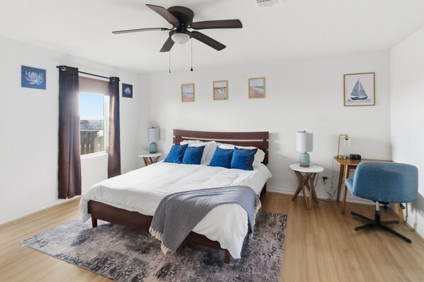 A bedroom with a bed, a ceiling fan, a desk, a chair, and a window with curtains.