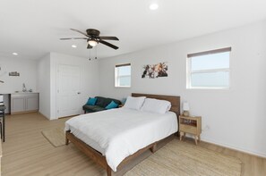 Une chambre à coucher avec un lit, un ventilateur de plafond, une table de chevet, un bureau et une fenêtre.