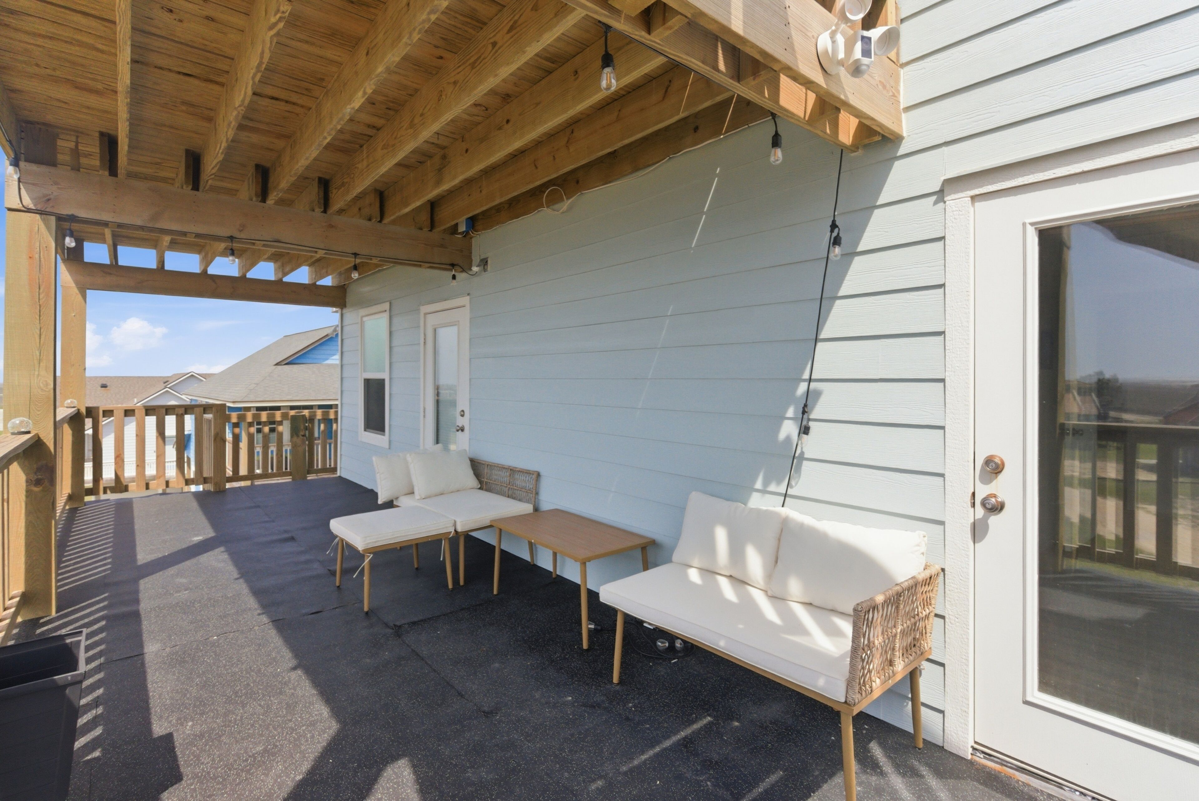 A covered patio with wooden furniture, a door, and a view of the sky.