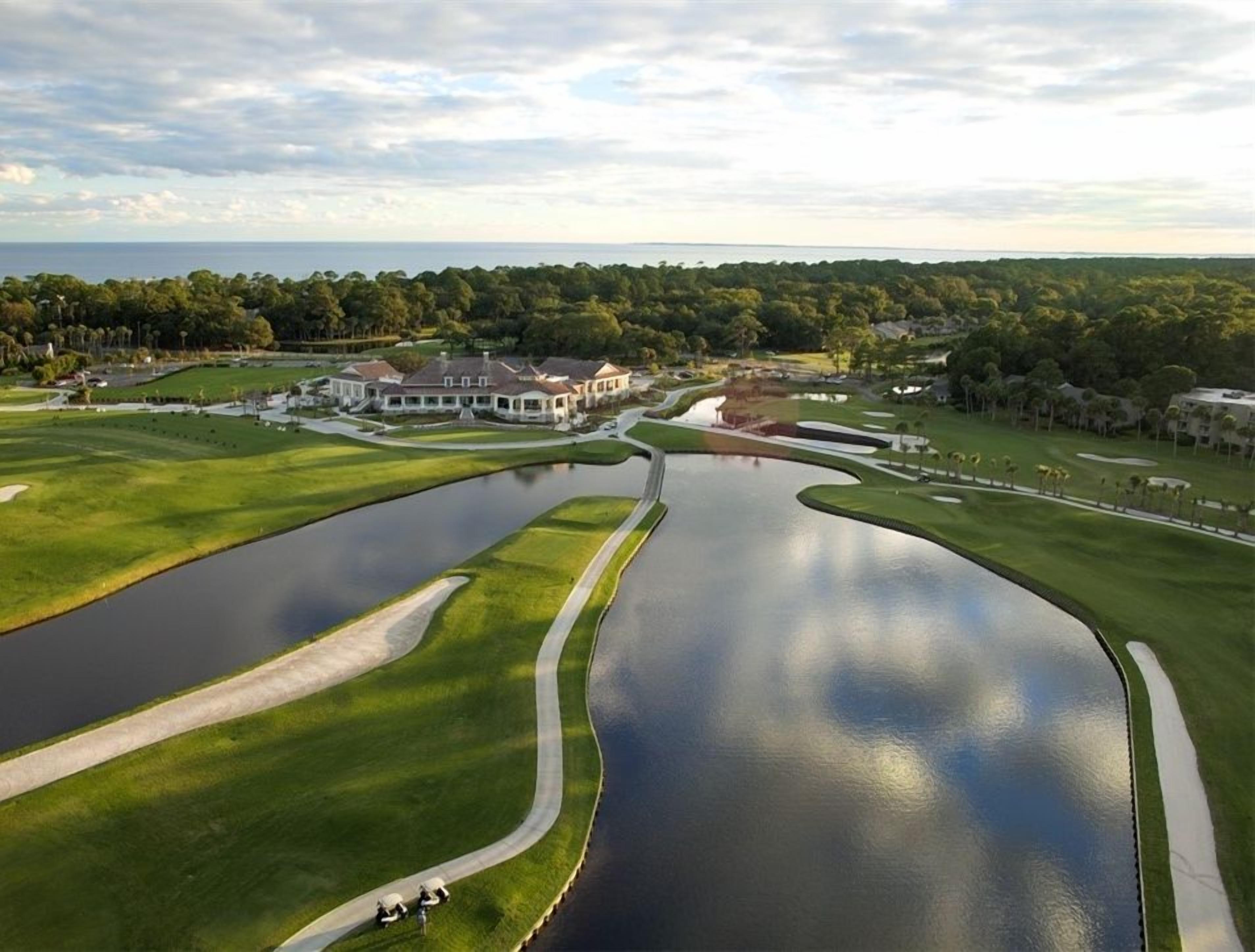Ein Golfplatz mit Teich, Clubhaus und umliegender Bepflanzung.